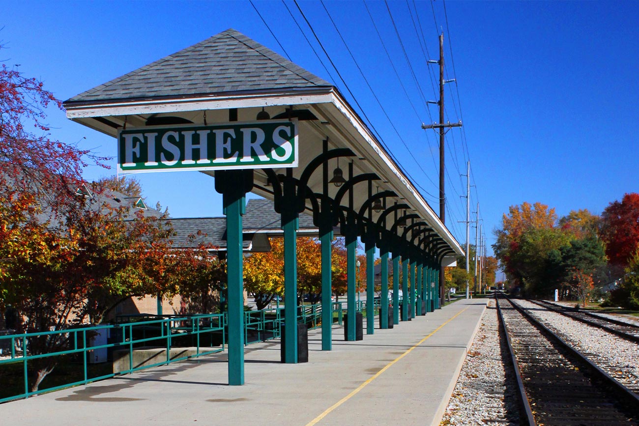 The image features a train station with a platform and a shelter, situated under a blue sky.
