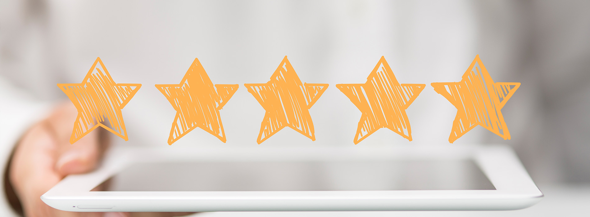 The image shows a tablet displaying five yellow star icons against a blurred background with an out-of-focus human hand holding the device.