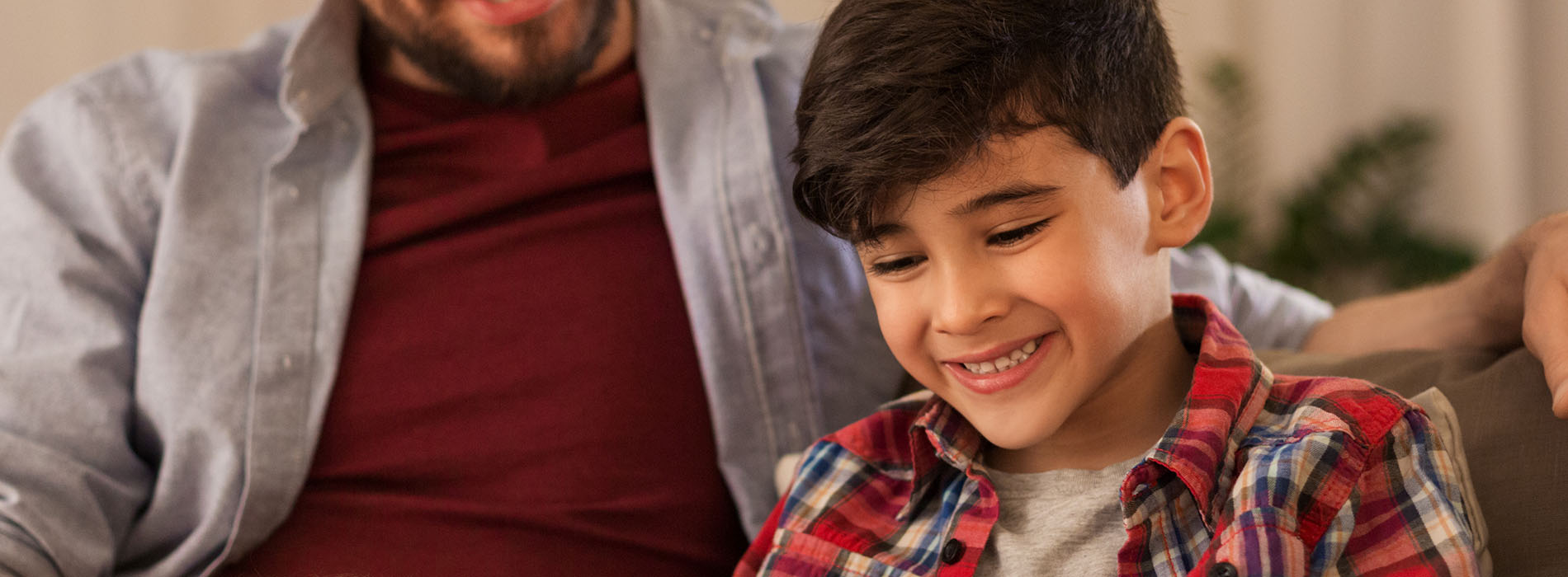 The image shows a young boy smiling at the camera while seated between two adults on a couch, with all three wearing plaid shirts.