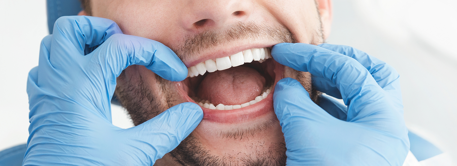 A man with his mouth open, wearing blue gloves and surrounded by dental equipment, possibly a dentist or oral surgeon at work.