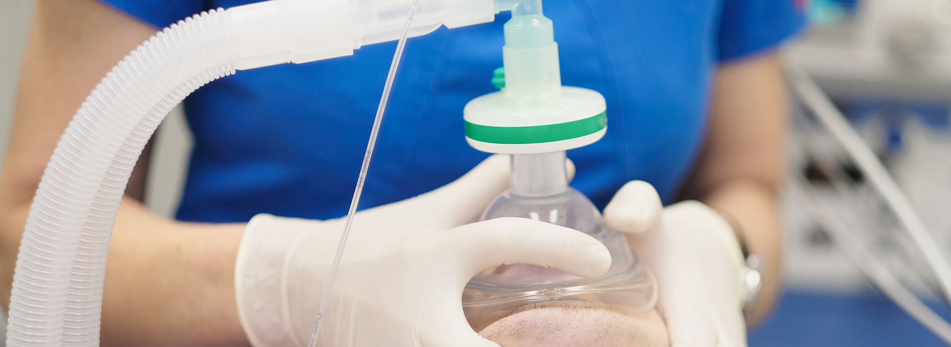 The image shows a person wearing gloves and a blue shirt performing a medical procedure on an animal, with a syringe attached to a tube connected to the animal's body, all set against a blue background.