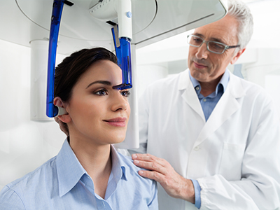 The image shows a medical professional assisting a patient with a head-mounted device, possibly for diagnostic purposes, with both individuals appearing focused on the task at hand.