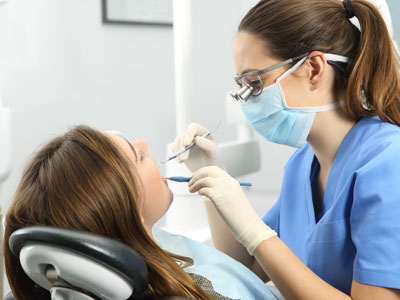 Dental hygienist performing oral examination on patient in dental chair.