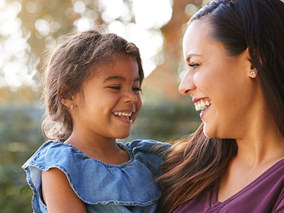 Woman and child smiling at camera, both outdoors during daylight.