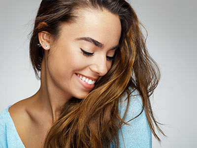 A woman with long hair smiling at the camera against a plain background.