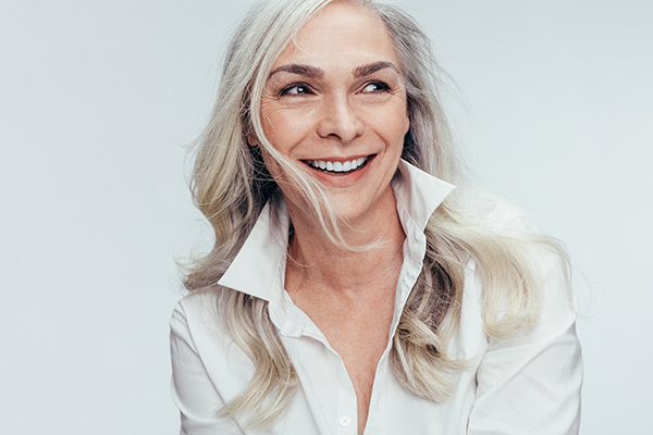 A woman with short hair and a smile, wearing a white top, against a plain background.