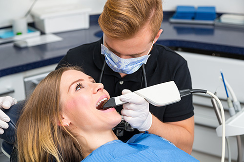 The image depicts a dental hygienist performing a cleaning procedure on a patient s teeth using a drill, with the patient sitting comfortably in a dental chair and wearing protective eyewear.