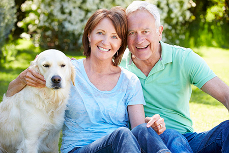 The image shows a man and a woman sitting outdoors with a dog on their laps, posing for a photo.