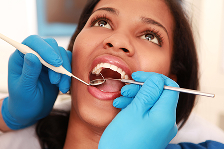 A woman undergoing dental treatment with a dentist using instruments and tools, wearing blue gloves and protective eyewear.