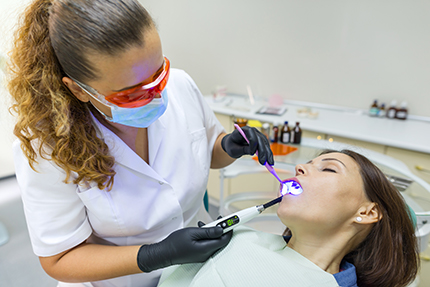A dental hygienist is cleaning a woman s teeth using an ultrasonic scaler while she sits in a dental chair.