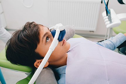 A young boy with a dental mask over his eyes, sitting in a dentist chair, being prepared for a dental procedure.