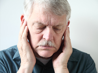 An elderly man with his hand on his ear, appearing to be in pain or discomfort.